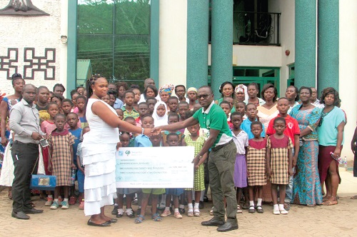 Mr Vincent Ampomah (right) presenting a dummy cheque to Mrs Grace Opoku-Gyamerah at a ceremony in Kumasi while some beneficiary students and other dignitaries look on