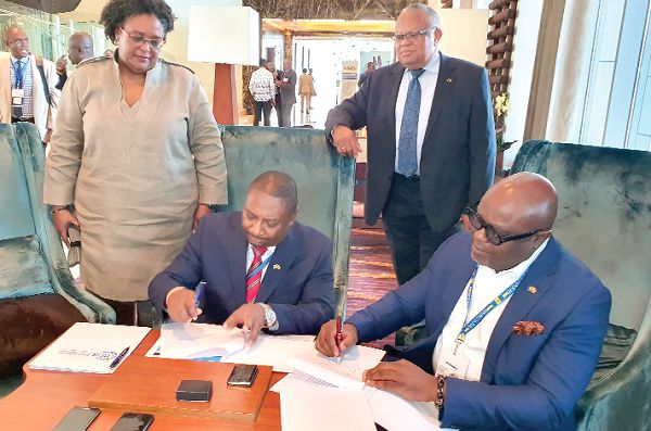 Nana Bambara-Abban (right) signing the agreement with Mr Dave Sahadath (3rd right). Looking on is Miss Mia Amor Mottley (left)